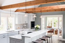 a chic dove grey contemporary kitchen with a two-level kitchen island, rich-tone woodne beams, pendant lamp and dark wooden stools