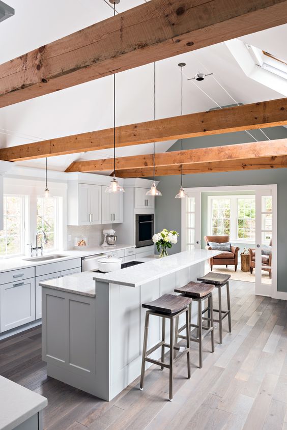 a chic dove grey contemporary kitchen with a two-level kitchen island, rich-tone woodne beams, pendant lamp and dark wooden stools