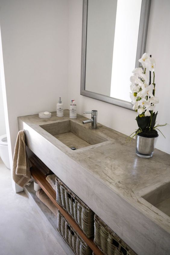 a concrete vanity with a double built-in sink and wooden shelves, mirrors in simple frames and basket drawers for storage
