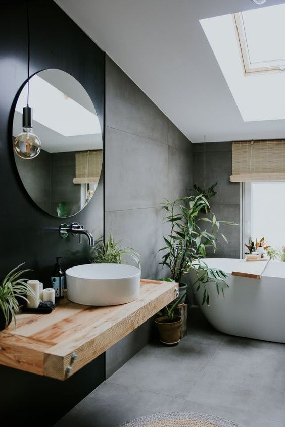 a contemporary attic bathroom with concrete walls and a floor, a black accent wall with a floating vanity and a round mirror