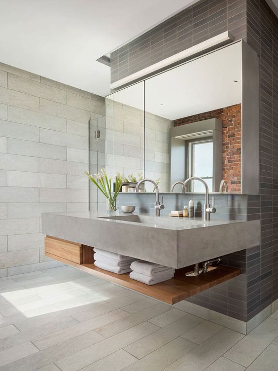 a contemporary bathroom clad with grey tiles and a grey concrete sink, wooden shelves and a large mirror
