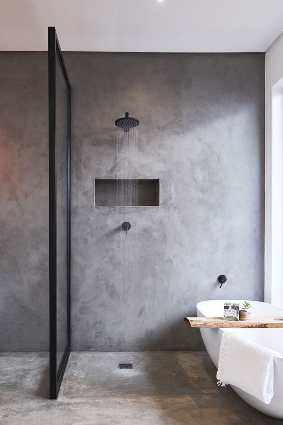 a contemporary bathroom of concrete, with a framed glass partition, an oval tub and black fixtures for a modern feel