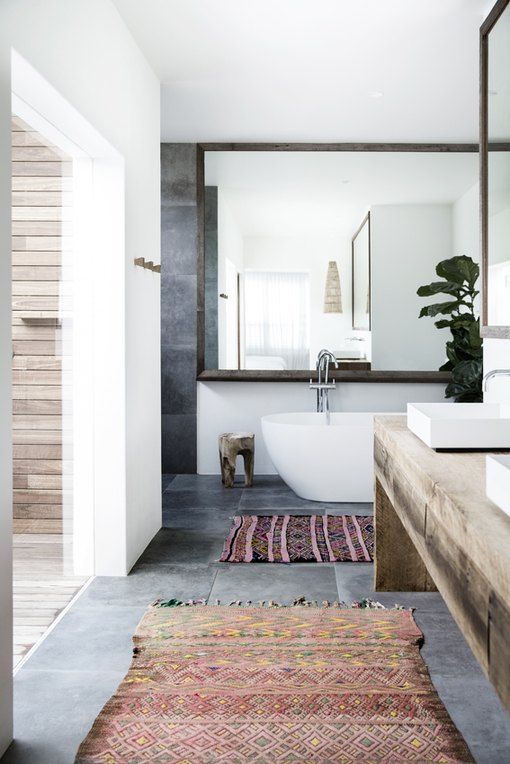 a contemporary bathroom with a concrete floor and walls, an oval tub, a double wooden vanity, square sinks and a large mirror wall