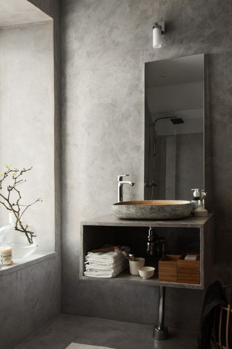 a contemporary concrete bathroom with a window, an open storage vanity, a sink carved of stone and a mirror