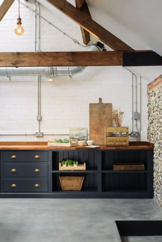 a contemporary kitchen with navy cabinets, a white brick wall, wooden beams and exposed pipes for an eye-catchy touch