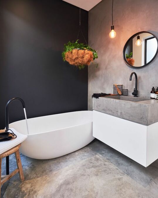 a contrasting bathroom with a black accent wall, floors, walls and a sink of concrete, black fixtures and a round mirror