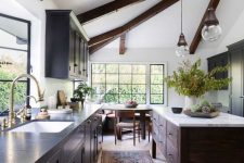 a contrasting kitchen with dark cabinets and a stained kitchen island, dark wooden beams, pendant lamps and lights