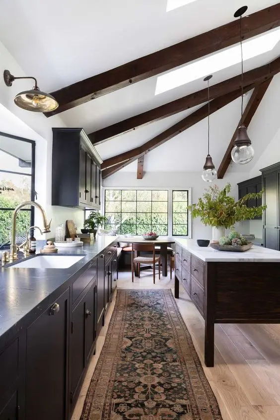 a contrasting kitchen with dark cabinets and a stained kitchen island, dark wooden beams, pendant lamps and lights