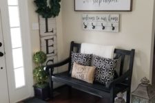 a cozy famrhouse entryway with a blakc vintage bench, candle lanterns, a sign and a colored rug