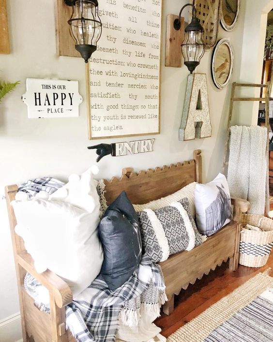 a cozy farmhouse entryway with a carved wooden bench, a gallery wall with signs and lamps, printed pillows and a blanket
