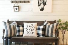 a cozy farmhouse entryway with a dark stained bench, printed pillows, some artworks and a large jute rug