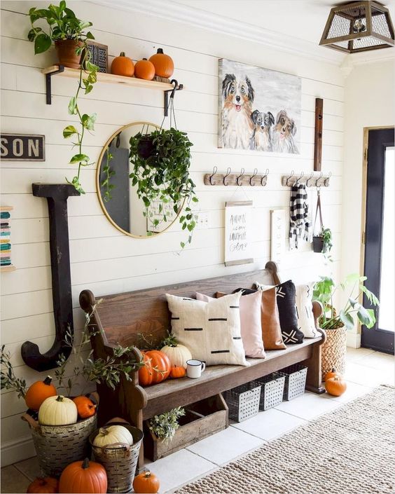 a fall farmhouse entryway with a wooden bench, some racks and shelves, a gallery wall and lots of pumpkins
