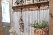 a farmhouse entryway with a corrugated steel wall, a rack with hooks, some metal lamps and a basket with greenery