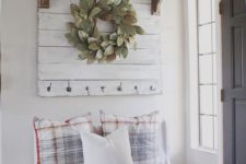 a farmhouse entryway with a white bench, checked pillows, a white rack, a wreath and a rack with white pumpkins for fall