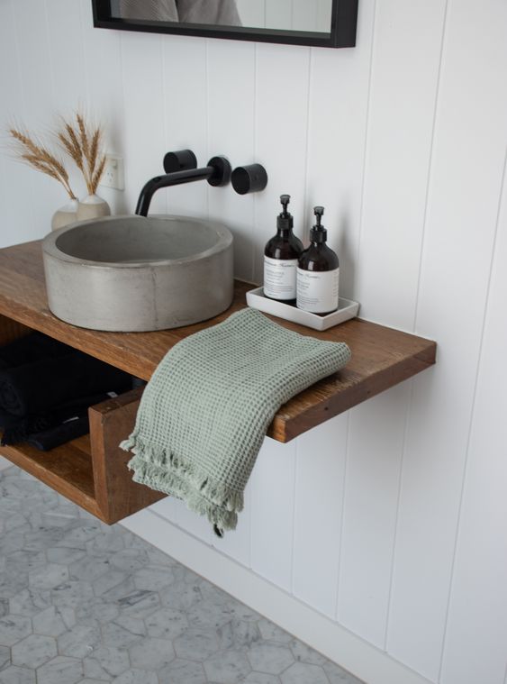 a floating wooden vanity with a round concrete sink and black fixtures is a bold and cool solution for a modern bathroom