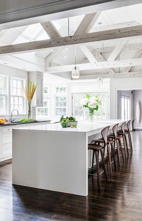 A light filled kitchen with whitewashed wooden beams, skylights and a large kitchen island plus wooden stools