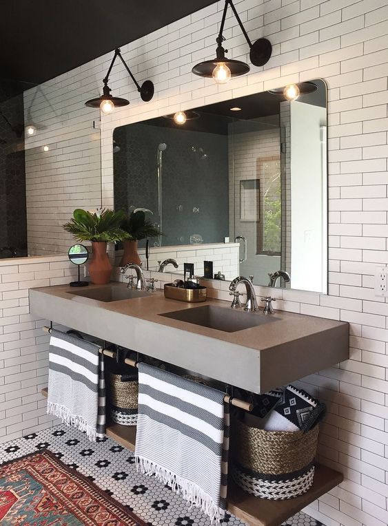 a mid-century modern bathroom clad with white tiles, a concrete floating vanity, black sconces and a large mirror plus baskets for storage