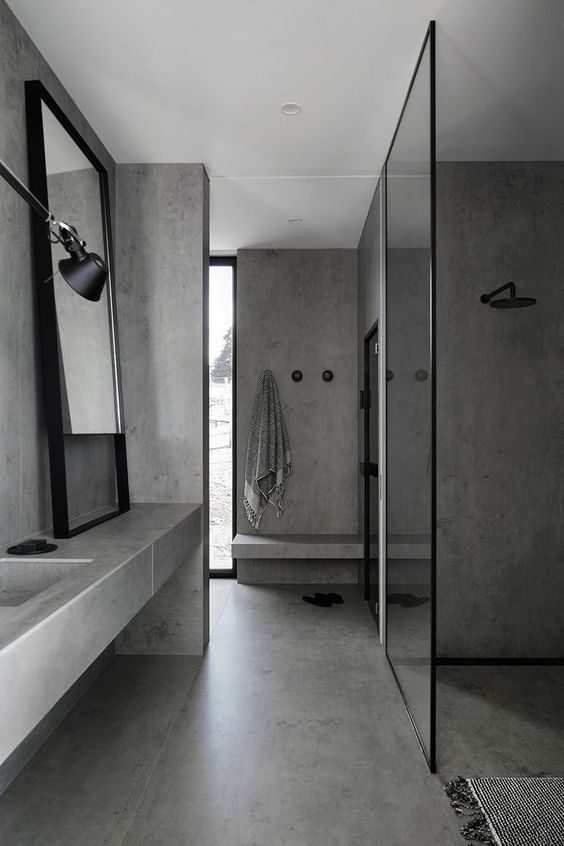 a minimalist bathroom fully made of concrete, with a concrete vanity, glass partitions, a framed mirror and a large window