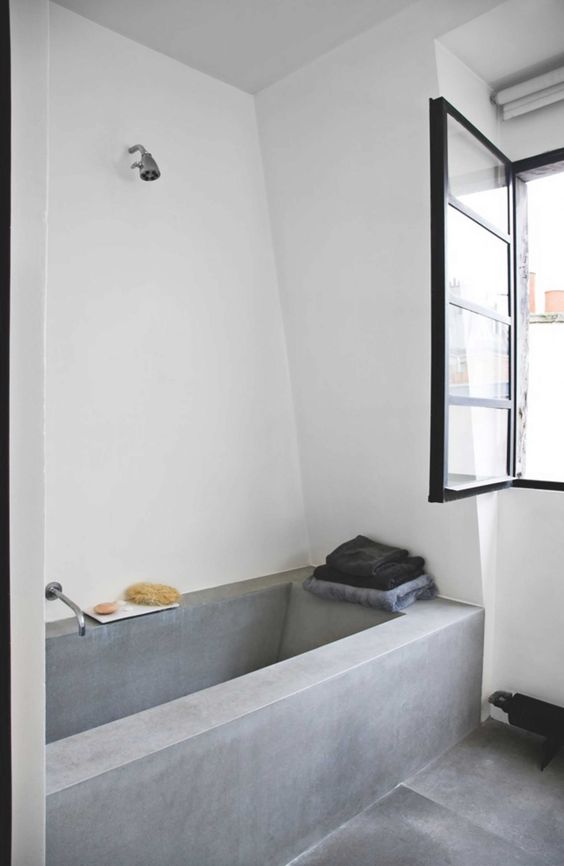 a minimalist bathroom with a concrete tub and a floor, a window for natural light and simple fixtures is cool
