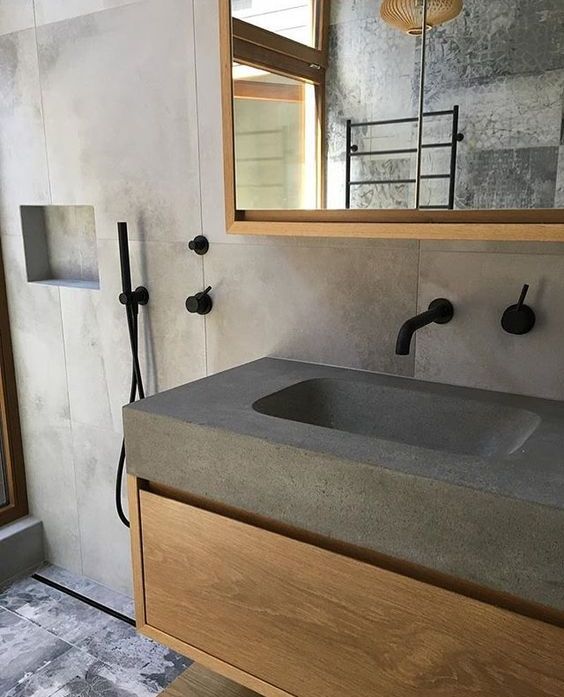 a minimalist concrete bathroom with a concrete countertop and a sink plus items of light stained furniture