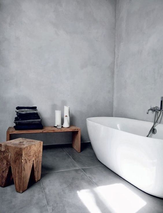 a minimalist concrete bathroom with rough wooden furniture and a stylish bathtub, it's welcoming and airy