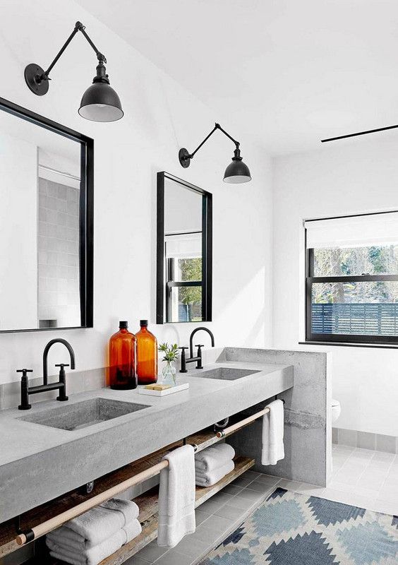 A modern bathroom with a built in concrete vanity and a half wall, catchy black sconces, black fixtures and mirrors in black frames