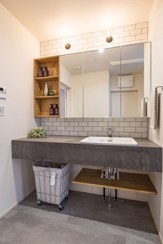 a modern bathroom with white subway tiles, a concrete vanity with a sink, mirror and wooden storage cabinets