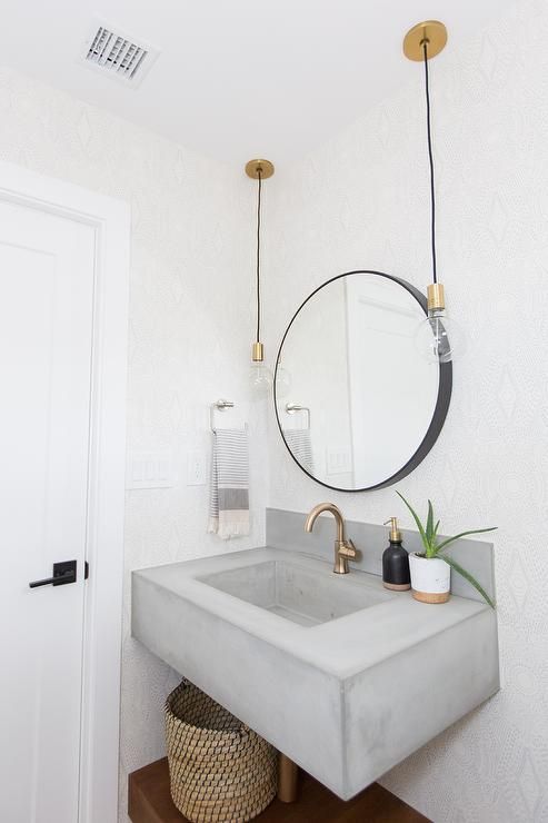 a modern bathroom with white tiles on the walls, a floating concrete sink, a round mirror, bulbs hanging down and a basket for storage