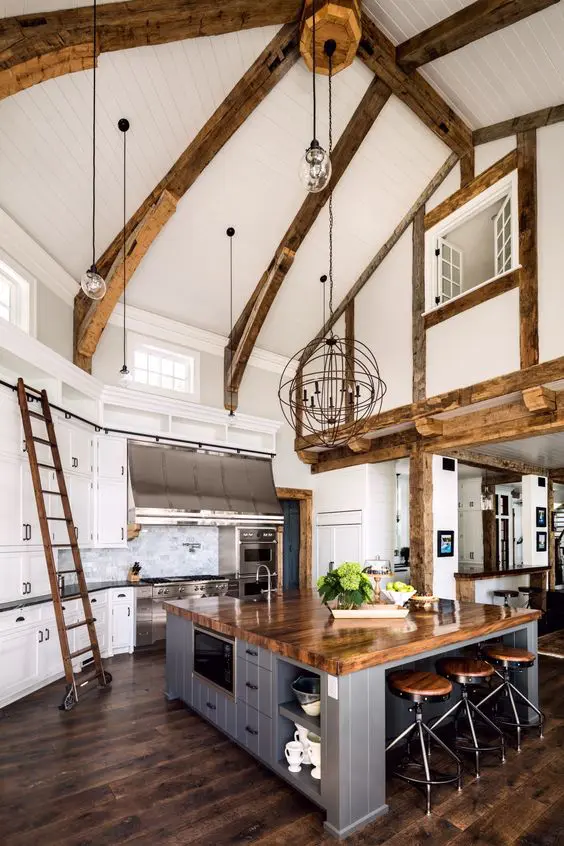 a modern farmhouse kitchen with white cabinetry, a grey kitchen island, wooden beams and countertops and pendant lamps