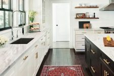 a modern farmhouse kitchen with white cabinets, a black kitchen island, wooden beams, a bright rug and gold touches is wow
