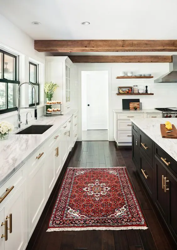a modern farmhouse kitchen with white cabinets, a black kitchen island, wooden beams, a bright rug and gold touches is wow