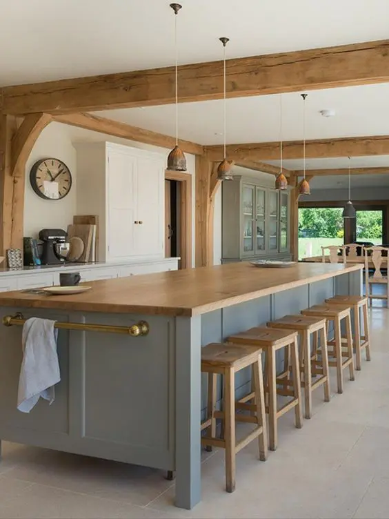 a modern farmhouse kitchen with white cabinets and a blue kitchen island, wooden beams and stools, pendant lamps for eye-catchiness
