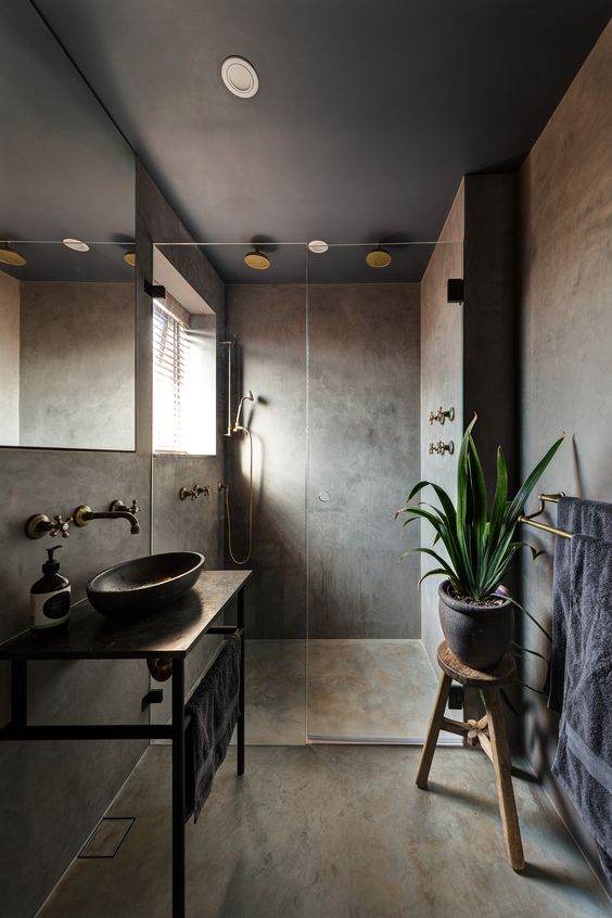 A moody concrete bathroom with a wall mounted vanity and a round sink, a wooden stool and a window in the shower plus vintage fixtures