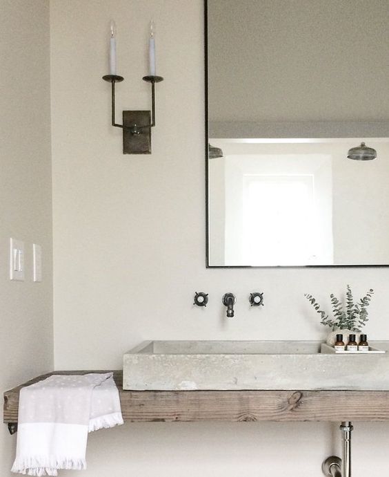 a neutral bathroom with a floating wooden vanity, a concrete sink, a mirror in a metal frame and simple fixtures looks relaxing