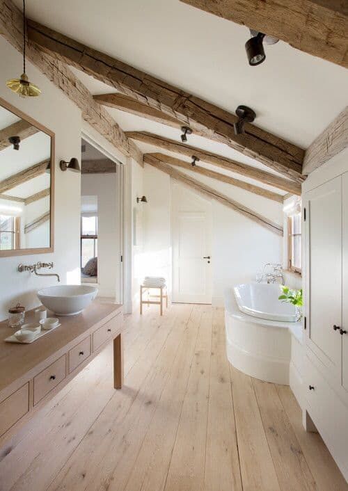 a neutral farmhouse bathroom with a large vanity, wooden beams on the ceiling, a large storage unit and a built-in tub
