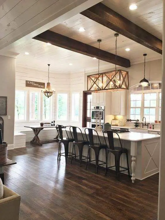 a neutral farmhouse kitchen with grey cabinetry, dark chairs and a table, pendant lamps and a wooden chandelier
