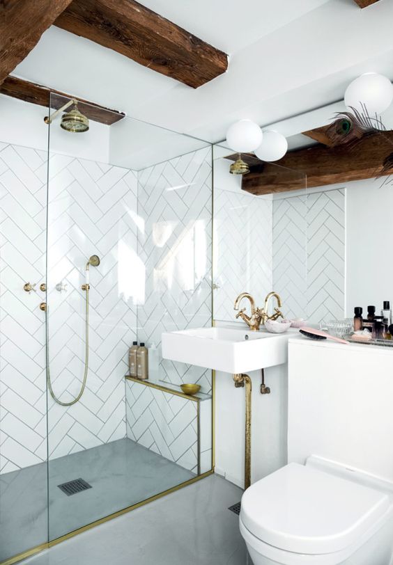 a neutral modern bathroom with white tiles, dark stained beams and gold fixtures plus white appliances