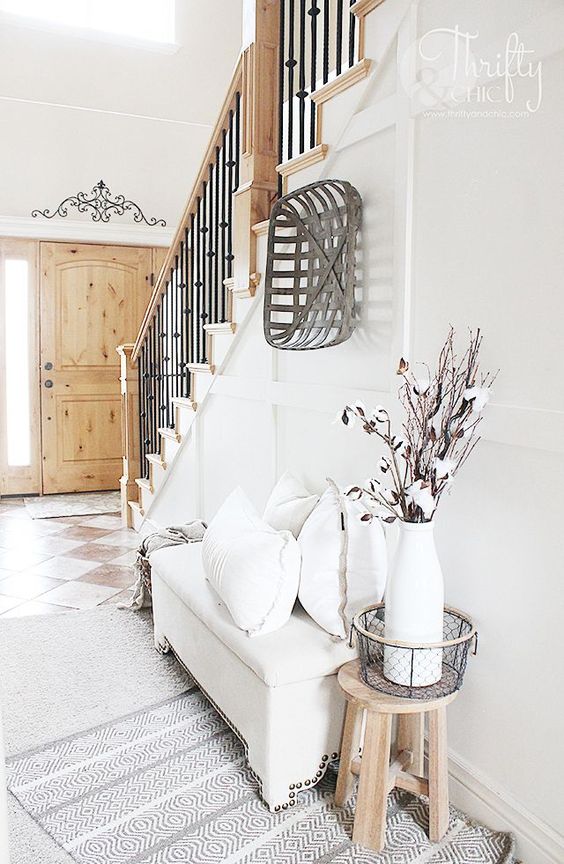 a neutral modern farmhouse entryway with a white upholstered bench, a wooden basket and some cotton branches in a vase