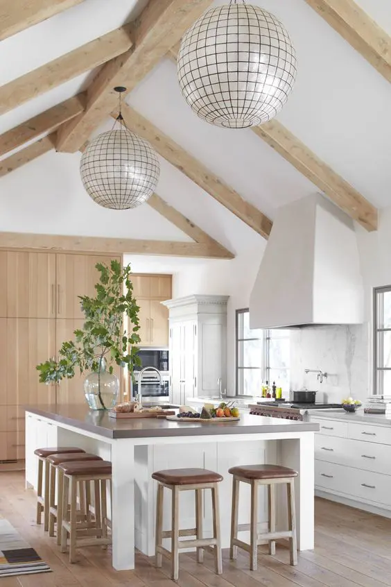 a neutral modern farmhouse kitchen with white cabinets and a kitchen island, a marble backsplash, light-colored wooden beams and sphere lamps