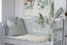 a neutral vintage farmhouse entryway with a grey bench, a vintage poster as an artwork, a rack and a pillow
