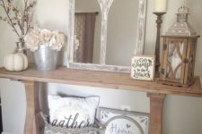a rustic console table with a metal bucket, a mirror in a vintage frame, a pumpkin and a woven basket with a pillow