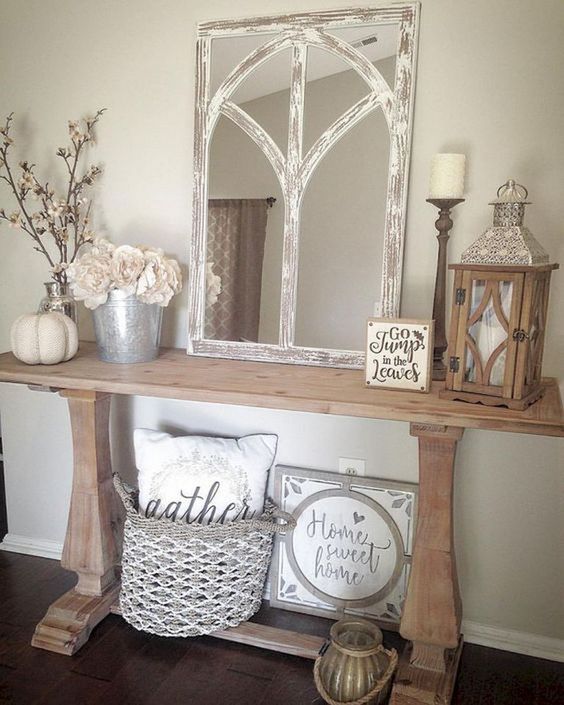 a rustic console table with a metal bucket, a mirror in a vintage frame, a pumpkin and a woven basket with a pillow