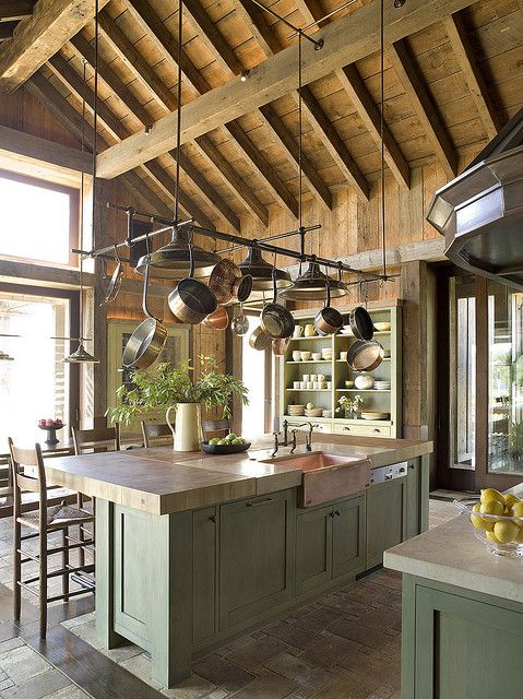 a rustic kitchen with green cabinetry, wooden and stone countertops, a wooden ceiling with beams is a chic space