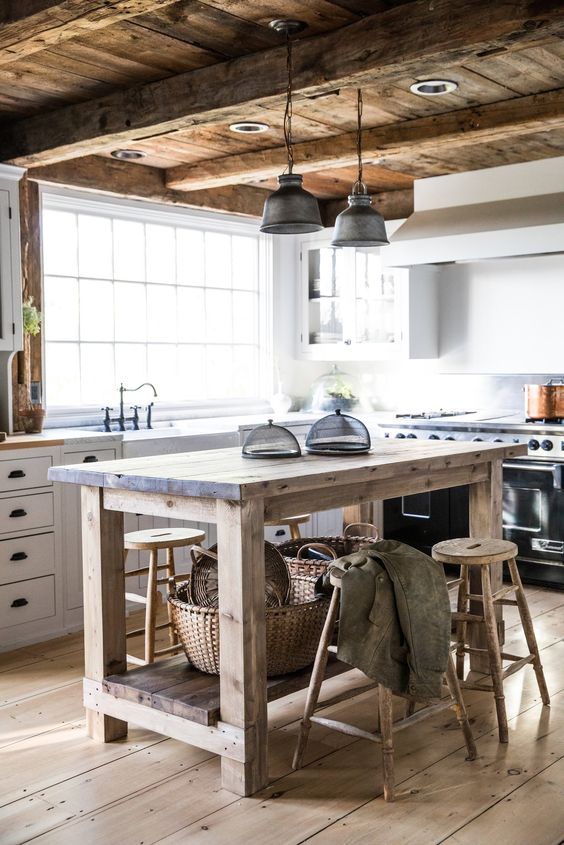 a rustic kitchen with white cabinetry, a rough wooden kitchen island, wooden stools, a wooden ceiling and beams, pendant lamps is very cozy
