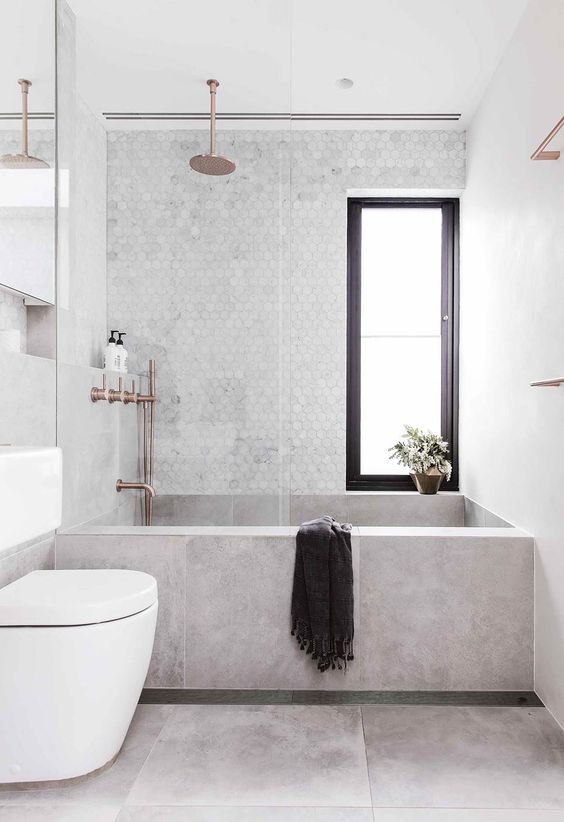 a stylish contemporary bathroom with a concrete wlal and bathtub, a marble penny tile wall and metallic fixtures