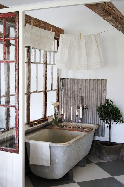 a vintage industrial bathroom with a concrete tub, shabby chic windows, some potted plants and candles