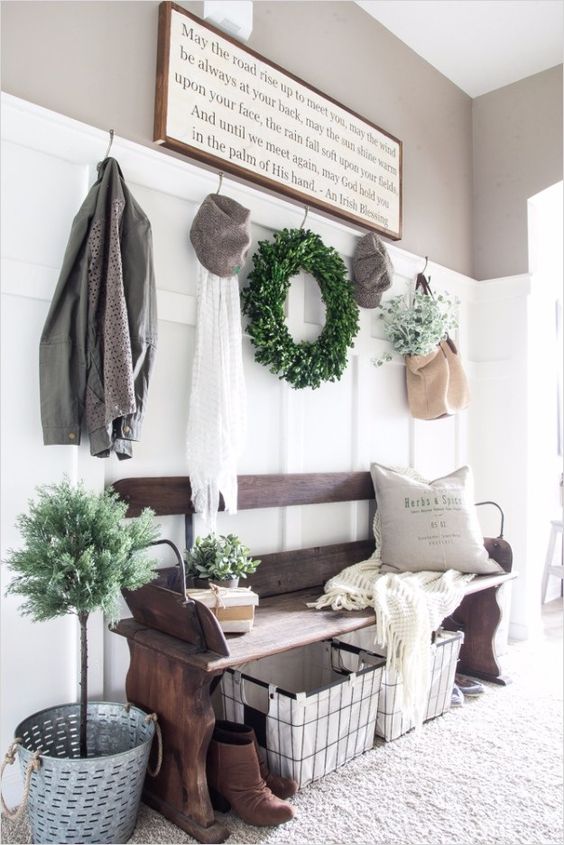 a welcoming farmhouse entryway with a weathered wooden bench, a wire basket, a sign, some decor and a boxwood wreath