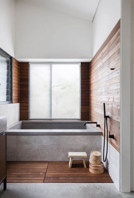 a zen Japanese bathroom with a bathtub clad with concrete and tiles, stained wood on the floor and walls is welcoming