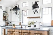 an airy and chic white kitchen with a wooden kitchen island and wooden beams on the ceiling plus refined vintage lamps on them
