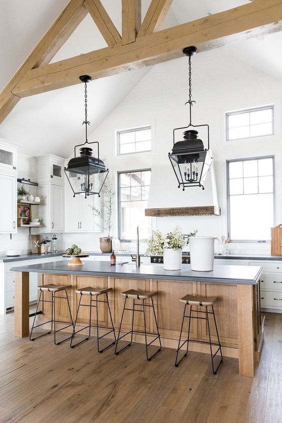 an airy and chic white kitchen with a wooden kitchen island and wooden beams on the ceiling plus refined vintage lamps on them